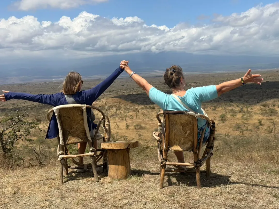 Two guests stretching out their arms on bush chairs above the plains at Osiligilai